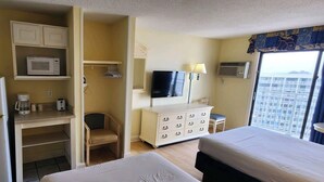 A hotel room with a bed, a desk with a chair, a microwave, a coffee maker, a television, and a dresser.