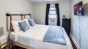 Un dormitorio ordenado con cama, mesita de noche y televisor montado en la pared.