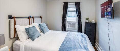 A neatly arranged bedroom with a bed, bedside table, and a TV mounted on the wall.
