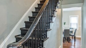 Una escalera con barandillas oscuras y un pasamanos, que conduce a un comedor con mesa y sillas.