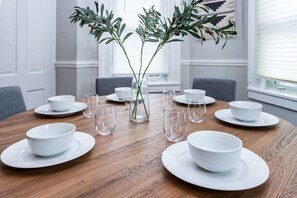 A dining table set with white plates, bowls, and glasses, surrounded by chairs.