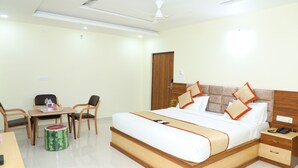 A hotel room with a large bed, wooden headboard, bedside table, and a desk with chairs. - Hotel 8th Mile Suites (Bengaluru)