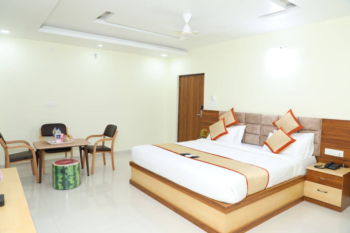 A hotel room with a large bed, wooden headboard, bedside table, and a desk with chairs.