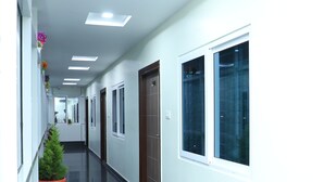 A long, narrow hallway with white walls, black tiled floors, and several potted plants. - Hotel 8th Mile Suites (Bengaluru)