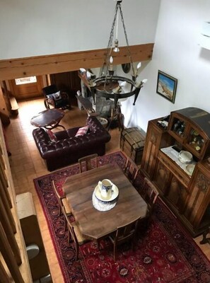 Un salon chaleureux avec une table à manger en bois, un tapis rouge à motifs, un canapé en cuir et un meuble en bois orné d’objets décoratifs.