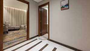 A hotel hallway with a striped floor, a door leading to a room with a bed and a chair, and a painting on the wall. - Westin Mark Hotel (Madinah)