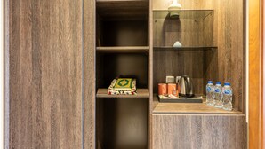 A wooden cabinet with shelves containing a book, mugs, a kettle, and water bottles. - Westin Mark Hotel (Madinah)