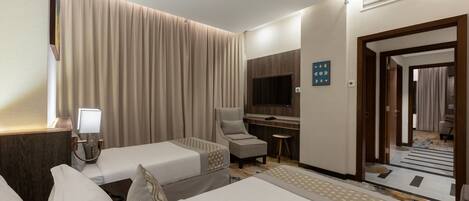 A hotel room with two beds, a desk, a TV, a chair, and a small table.