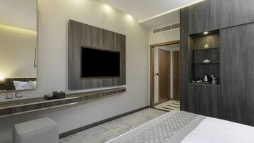 Una habitación de hotel moderna con una cama grande, un televisor montado, un tocador con espejo y un estante empotrado con artículos de aseo.