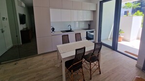 Una cocina moderna con armarios blancos, una mesa de comedor con sillas y un amplio ventanal corredero que da a un balcón con plantas.