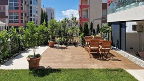 Un patio con terraza de madera, plantas en macetas y mobiliario exterior.