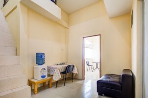 Una habitación pequeña y bien iluminada con una mesa de comedor, sillas, un dispensador de agua y un sofá.