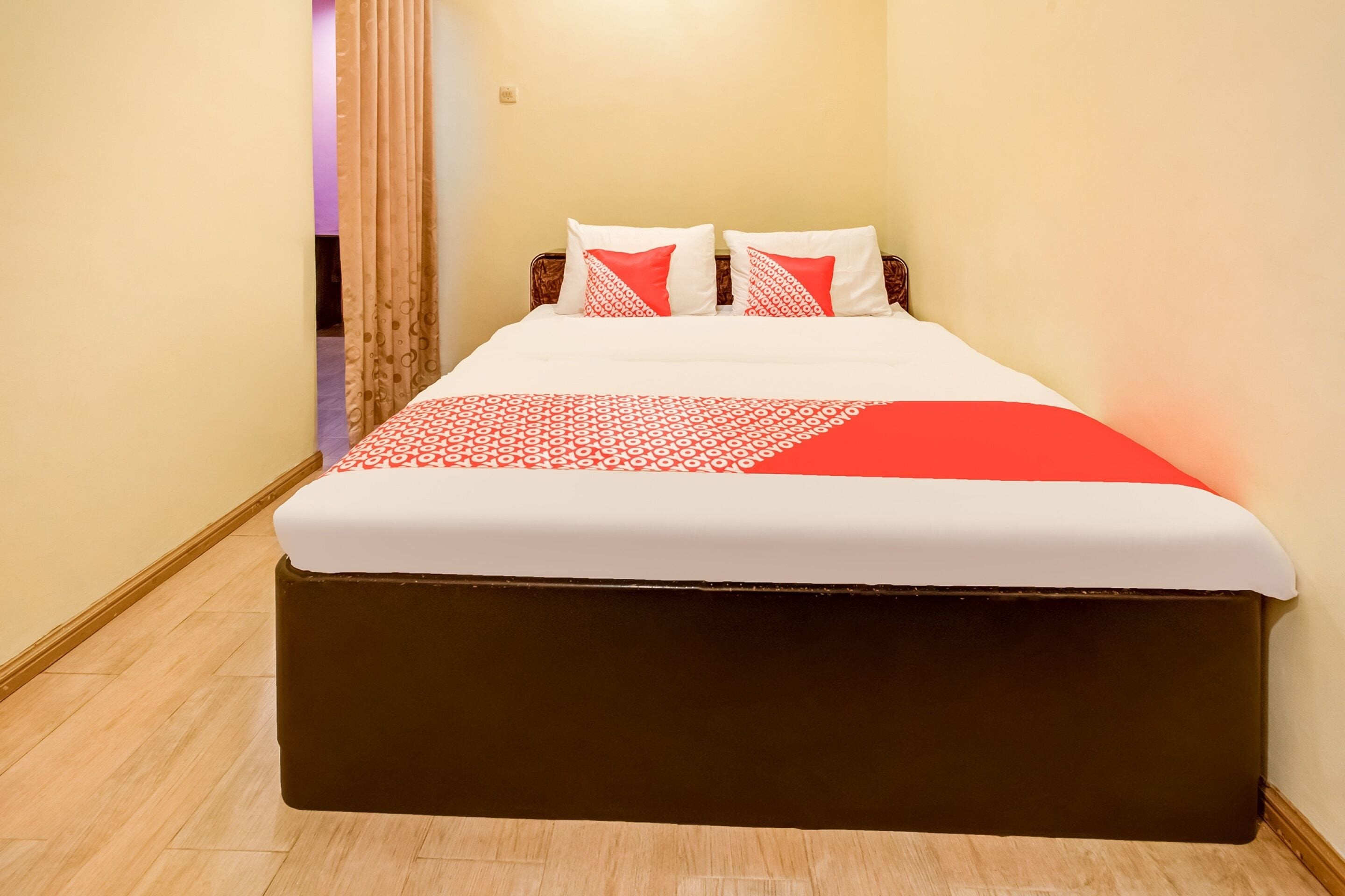Een net opgemaakt bed met een wit en rode sprei, twee kussens met rode en witte patronen, en een donkerbruin hoofdbord.