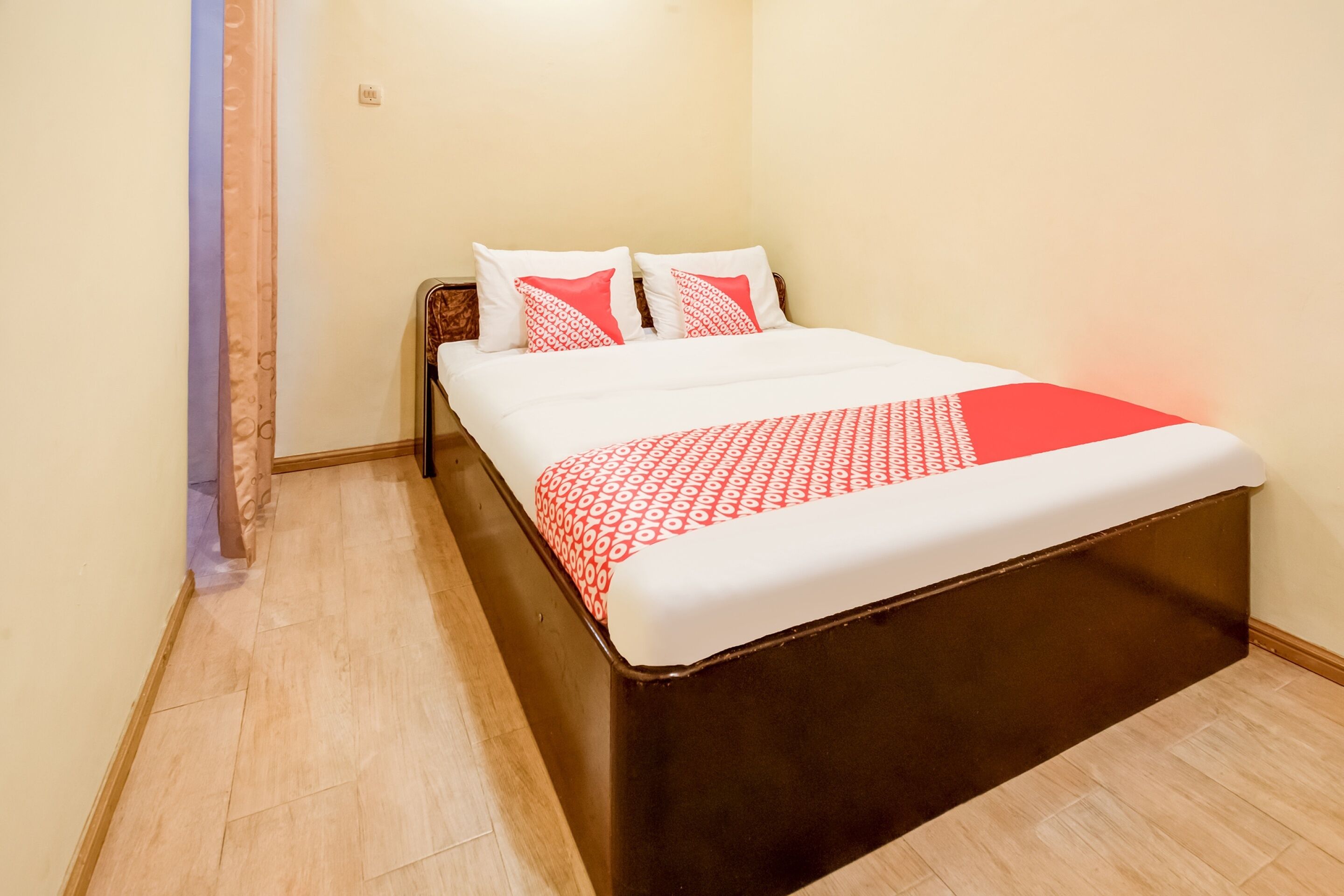 A neatly made bed with a patterned bedspread and pillows, a wooden headboard, and a light-colored floor.