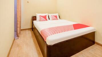 A neatly made bed with a patterned bedspread and pillows, a wooden headboard, and a light-colored floor.