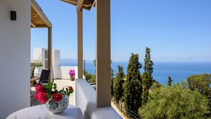 Un balcón con una mesa de mármol blanco, un jarrón de rosas rosadas y vistas al mar y al verdor.