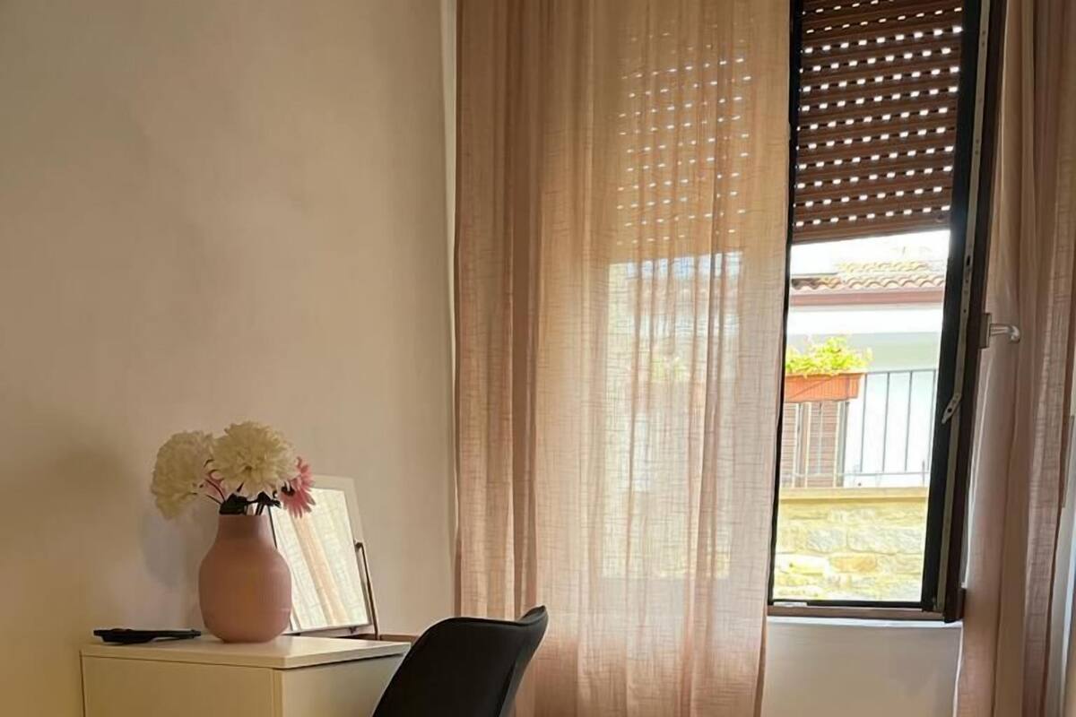 A hotel room with a bed, a desk with a computer, a chair, a small heater, and a window with curtains.