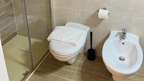 A bathroom with a glass shower enclosure, a toilet, a bidet, and a towel rack.