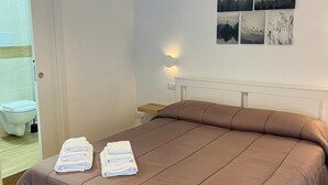 A neatly made bed with a brown cover, a bedside table, and a wall with four landscape paintings.