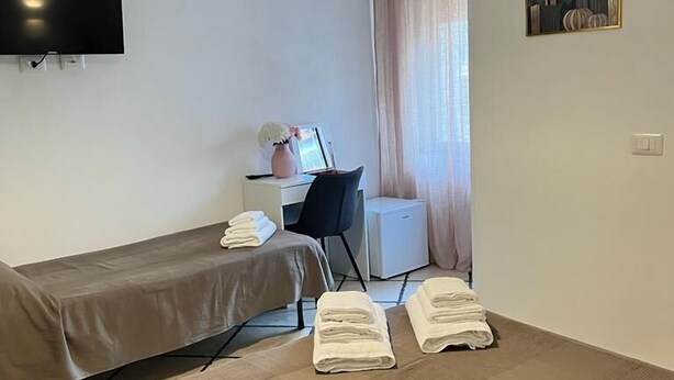 A small, neatly arranged room with a bed, a desk, a chair, and a TV mounted on the wall.