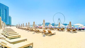 A beach with rows of sun loungers and umbrellas, a Ferris wheel, and modern buildings in the background. - bnbme | Address Beach Resort | 1 BDR (Dubai)