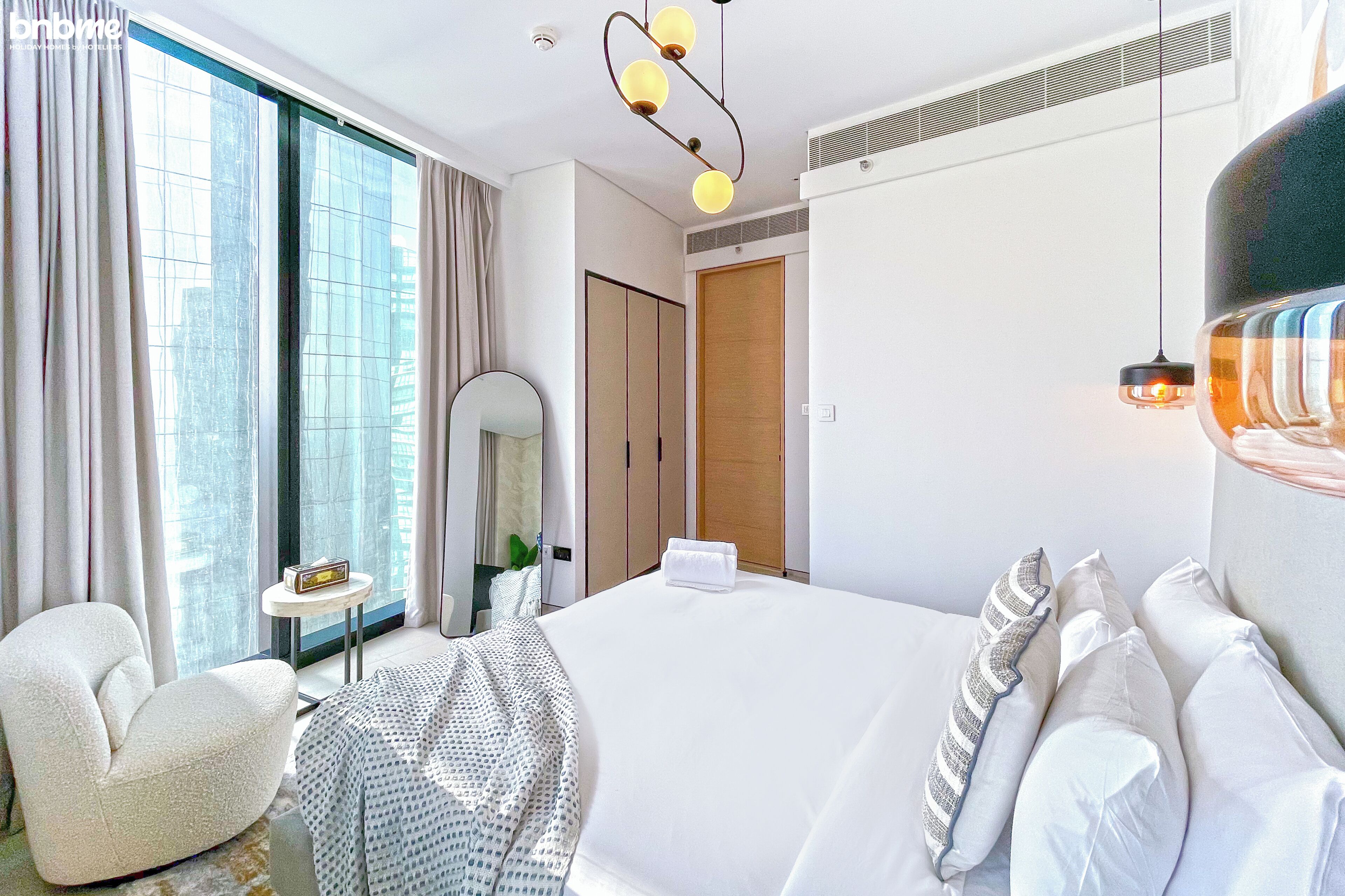 Hotelkamer met een groot bed, een zithoek met een stoel, een klein tafeltje, een spiegel en uitzicht op de stad door het raam.
