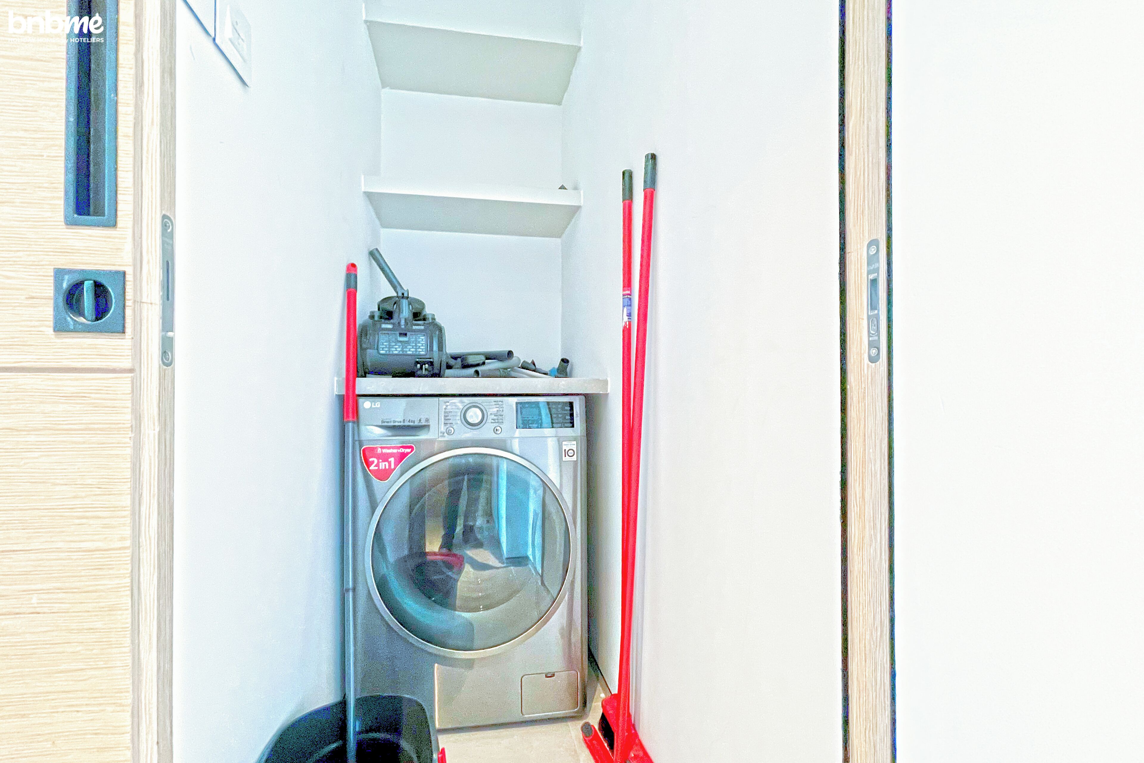 A compact laundry area with a washing machine, a small shelf, and a broom.