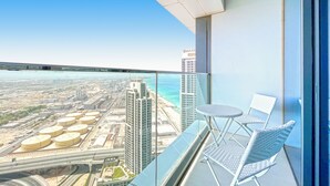 A high-rise balcony with a view of a cityscape, including industrial buildings and a beach. - bnbme | Address Beach Resort | 1 BDR (Dubai)