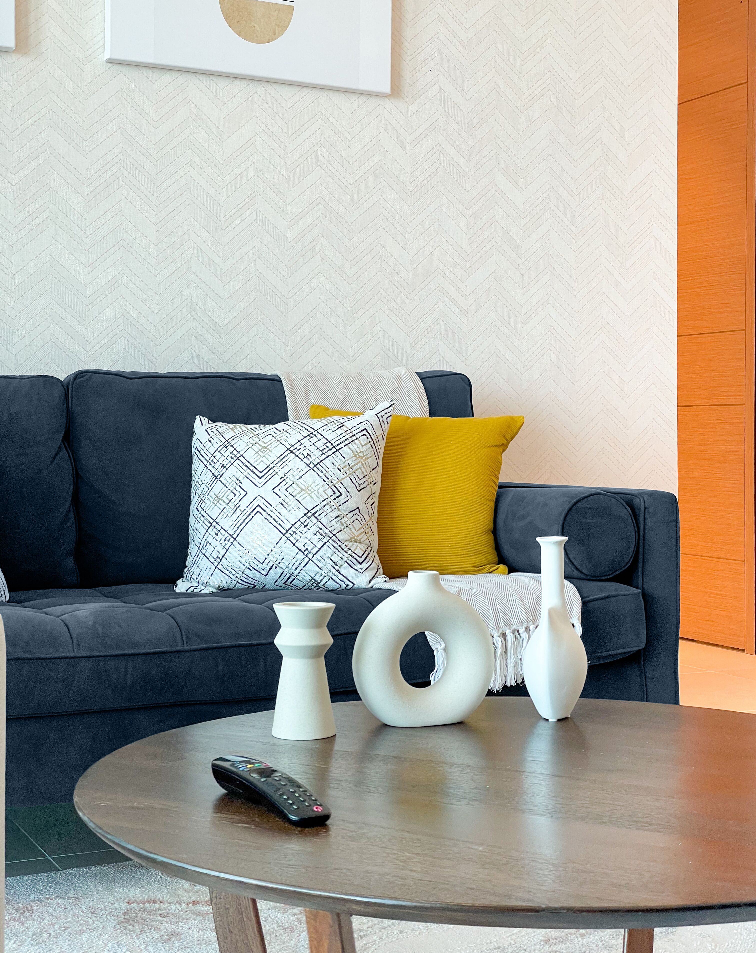 A modern living room with a dark blue sofa, a round coffee table, and decorative vases.