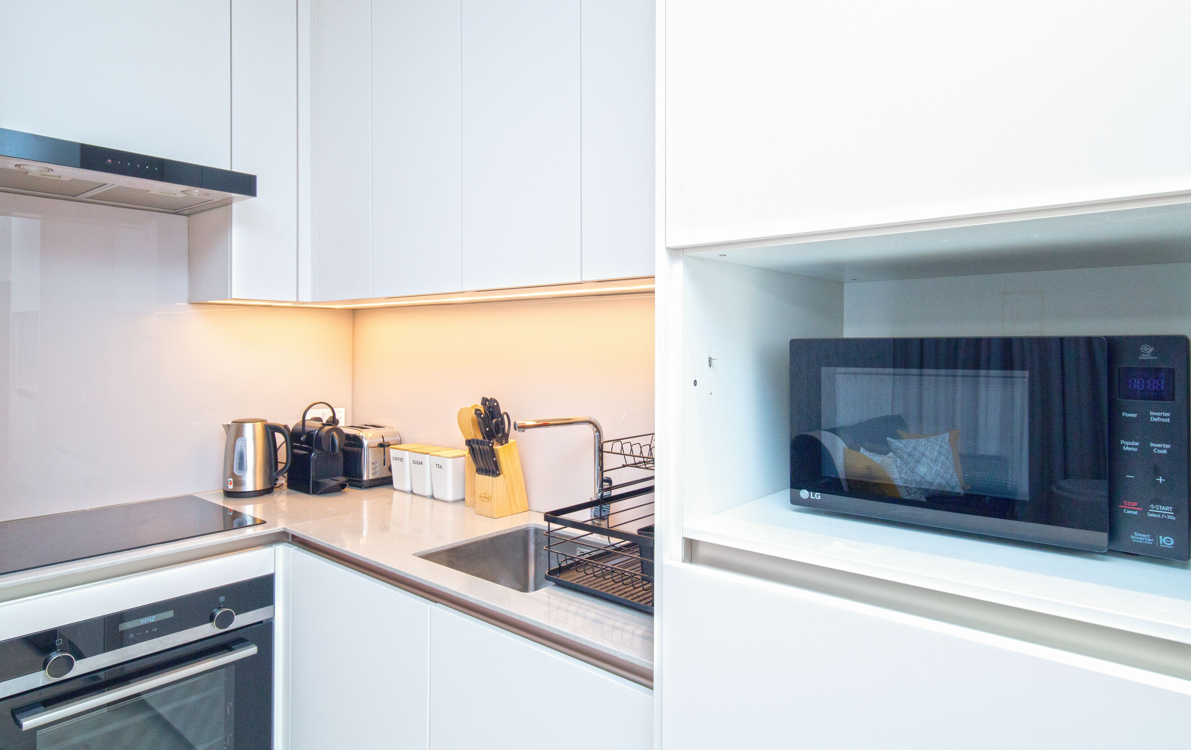 A modern kitchen with white cabinets, a built-in oven, a microwave, and a coffee maker.
