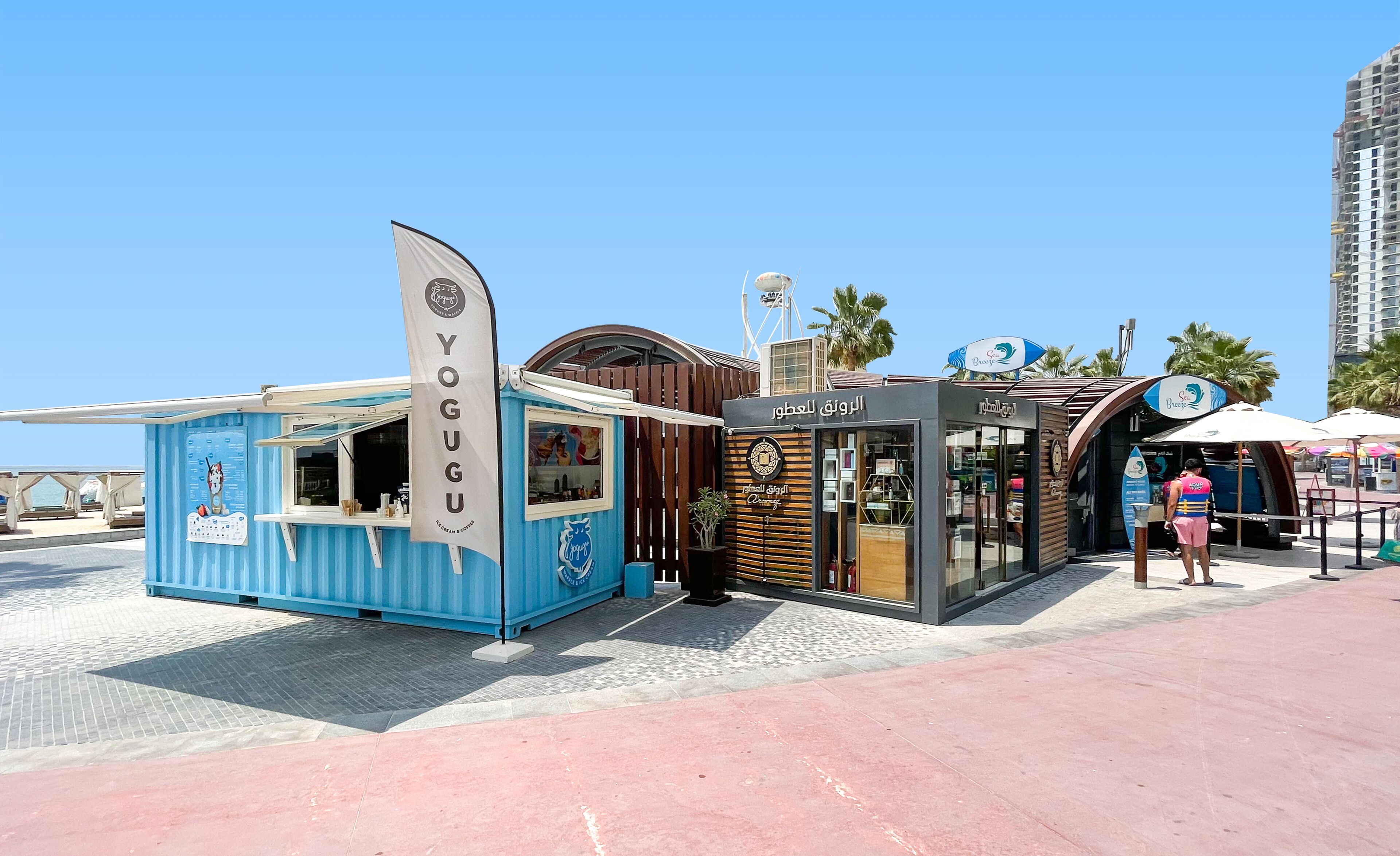 A blue kiosk with a sign reading "YOGU" and a modern building with Arabic signage.
