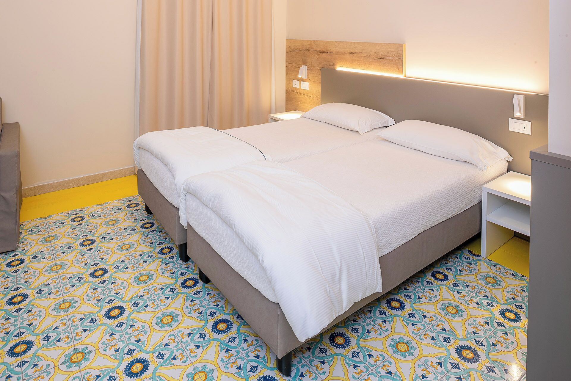Een hotelkamer met een bed, nachtkastjes en vloertegels met een patroon.