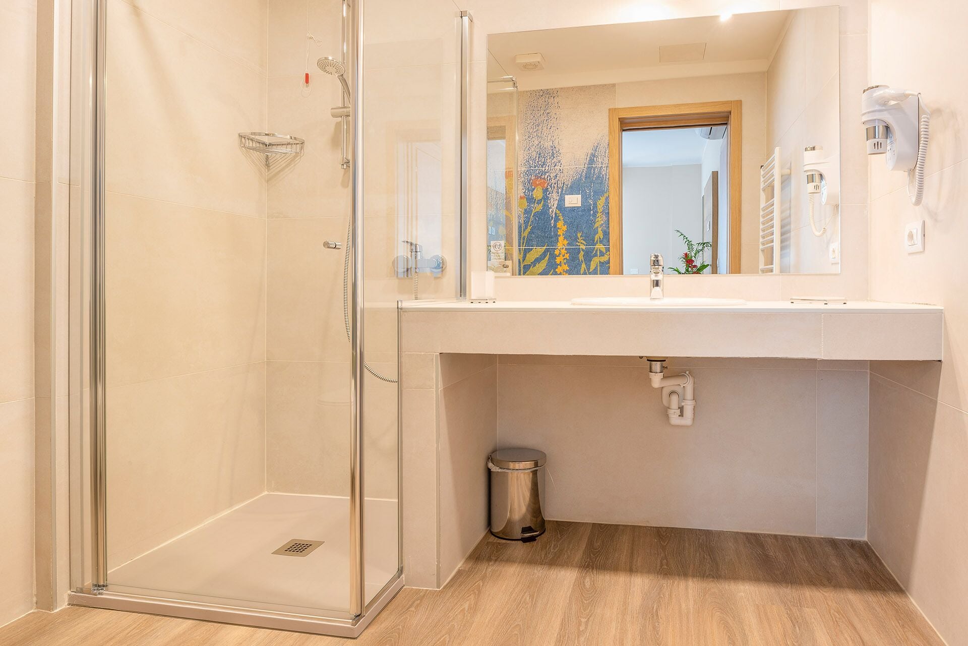 A bathroom with a glass-enclosed shower, a sink with a mirror above, and a trash bin.