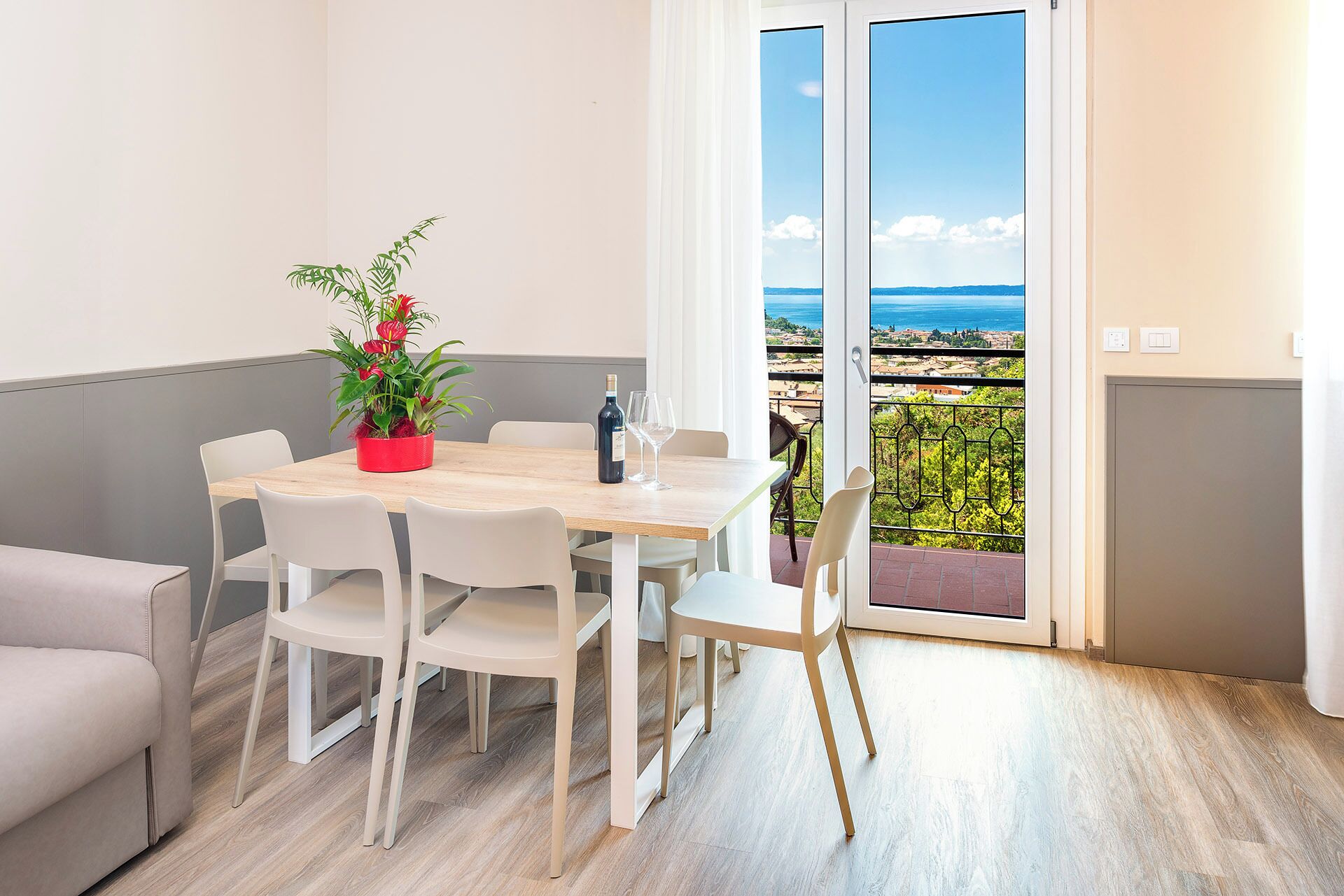 Een eetgedeelte met een tafel, stoelen, een potplant en uitzicht op de zee door een glazen deur.