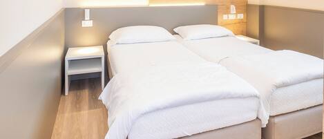 Een tweepersoonsbed met houten hoofdbord, nachtkastje en een wandlamp.