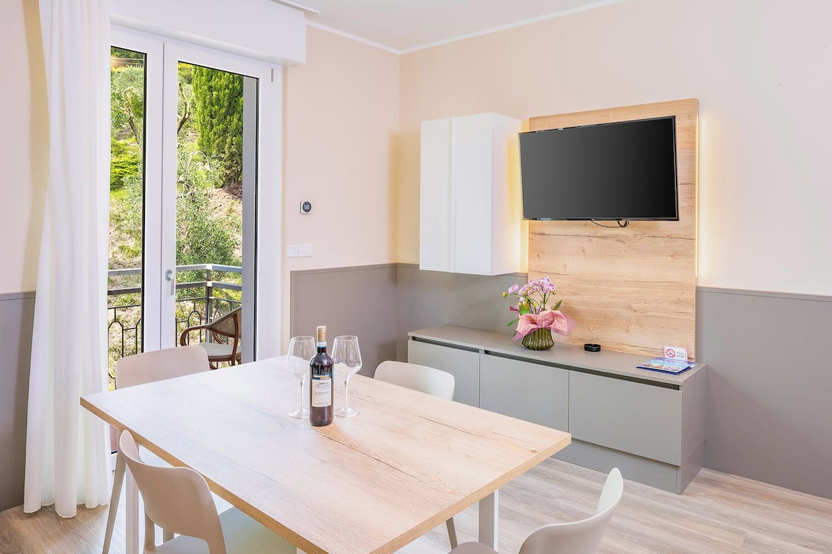 A modern kitchen with a TV, a dining table with chairs, and a view of greenery outside.