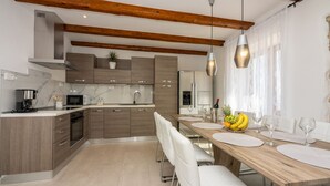 A modern kitchen with wooden beams, a dining area with a wooden table, white chairs, and a fruit bowl. - Villa Antani with heated pool, sauna and jacuzzi (Crikvenica)
