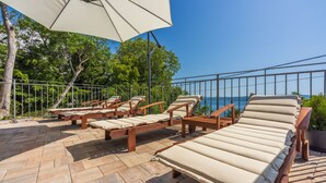 A terrace with lounge chairs and a large umbrella, overlooking a scenic view. - Villa Antani with heated pool, sauna and jacuzzi (Crikvenica)