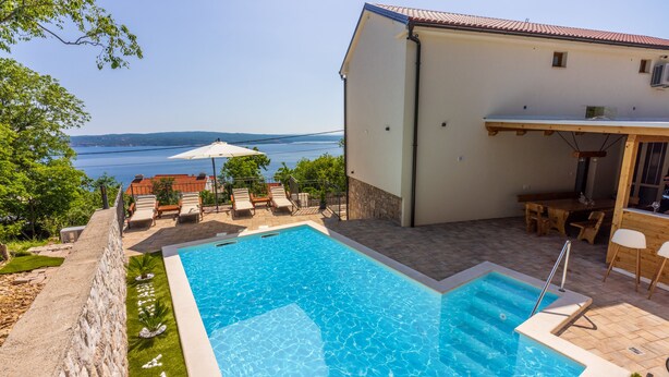 A swimming pool with a view of the sea, outdoor seating, and a building with a tiled roof. - Villa Antani with heated pool, sauna and jacuzzi (Crikvenica)