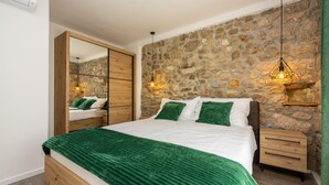 A bedroom with a stone wall, a wooden bed frame, a green bedspread, and two bedside lamps. - Villa Antani with heated pool, sauna and jacuzzi (Crikvenica)
