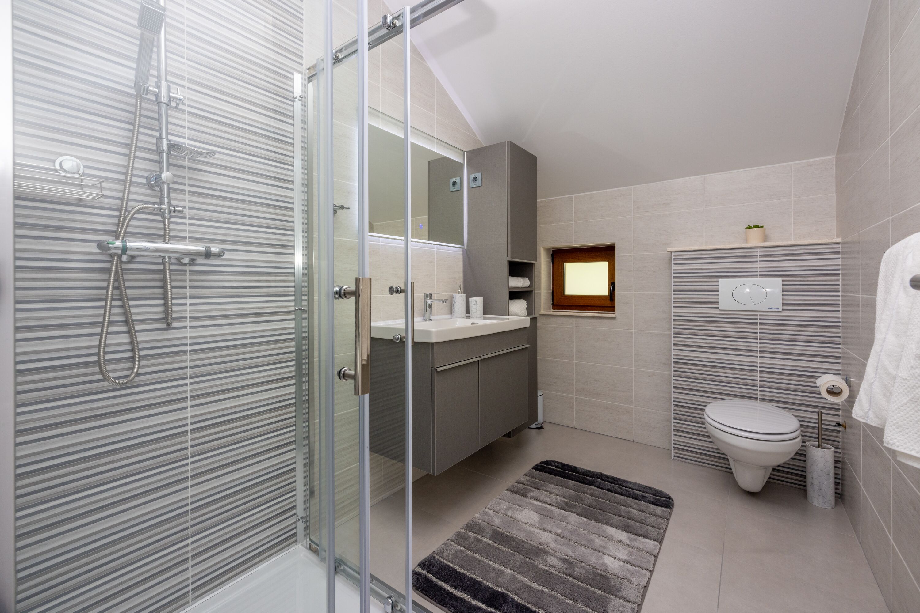 Ein modernes Badezimmer mit Duschkabine aus Glas, Waschbecken mit Spiegel, Toilette und Handtuchhalter.