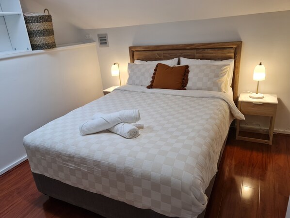 A neatly made bed with a checkered duvet, two bedside lamps, and a wooden headboard.