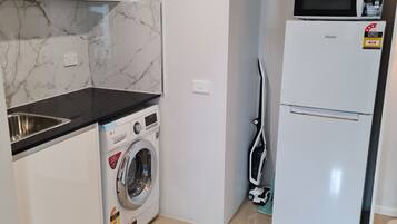 A compact kitchen with a washing machine, a microwave, and a refrigerator.