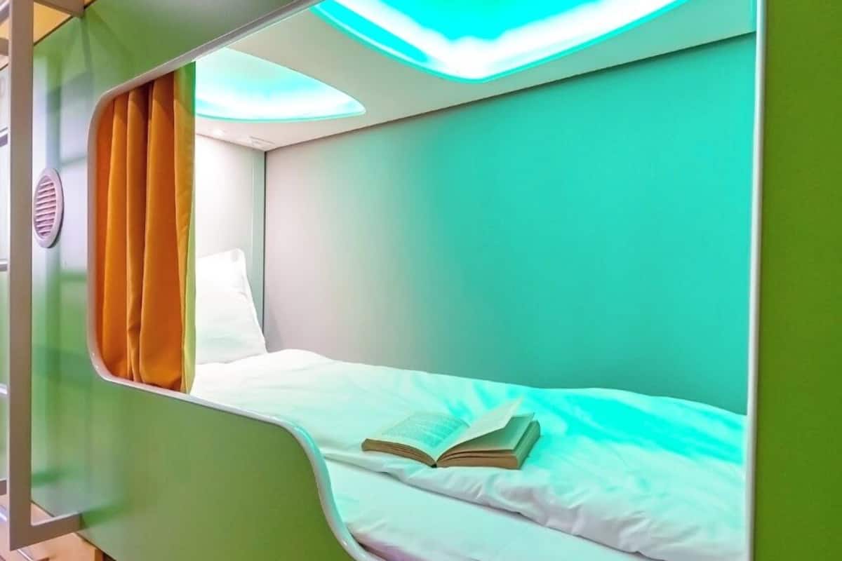 A bunk bed with a book on the lower bunk, a window with curtains, and a ventilation grille.
