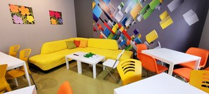 Una habitació de colors vives amb un sofà groc, taules blanques i cadires taronja.