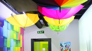 A hallway with colorful walls, a bright yellow chair, and an exit sign. - Green cube hostel (Sofia)