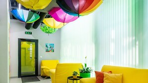 A brightly lit reception area with yellow sofas, a green plant, and colorful umbrellas hanging from the ceiling. - Green cube hostel (Sofia)