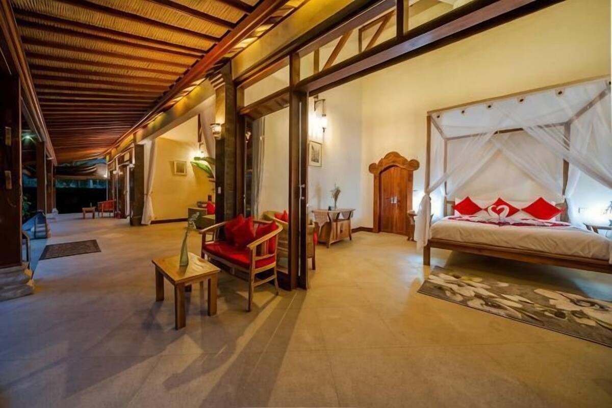 A hotel room with a bed, a red sofa, a wooden table, and a large window.