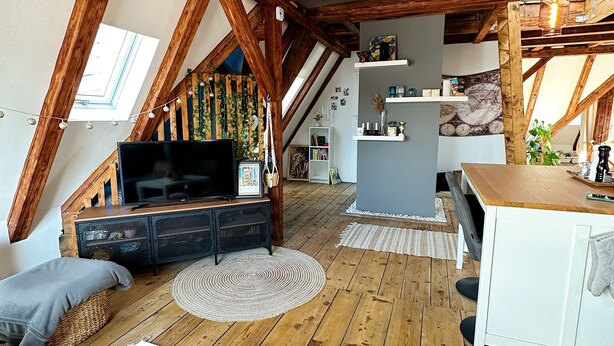 Ein Loft-Zimmer mit freiliegenden Holzbalken, einem Fernseher und einer Essecke mit Obstschale.
