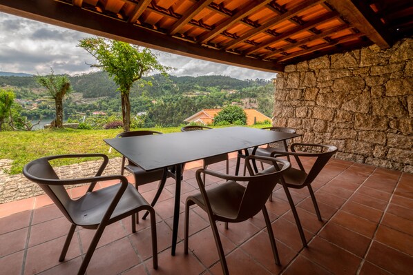 An outdoor patio with a table and chairs, a stone wall, and a view of a hilly landscape.